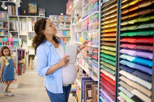 Pregnant woman, inspired painter standing by shelf with color paper sheets, for design, pastel and watercolor painting
