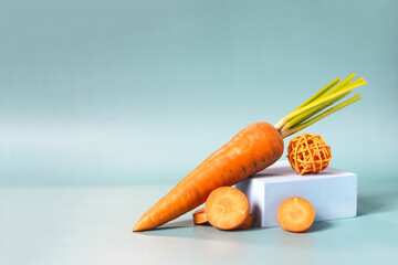 Bright carrots and carrot slices with a blue podium close-up on a blue background.