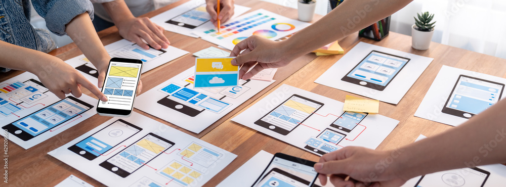 Poster Panorama shot of front-end developer team brainstorming UI and UX designs for mobile app on paper wireframe interface. User interface development team planning for user-friendly UI design. Scrutinize