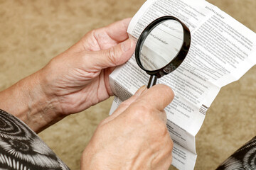 an elderly woman studies the instructions for the use of pills with a magnifying glass