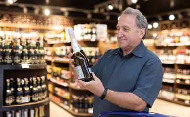 Mature man choosing fine bottle of champagne in supermarket