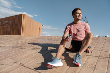 A male runner drinks clean water from a sports bottle, rests during fitness classes on the street,...