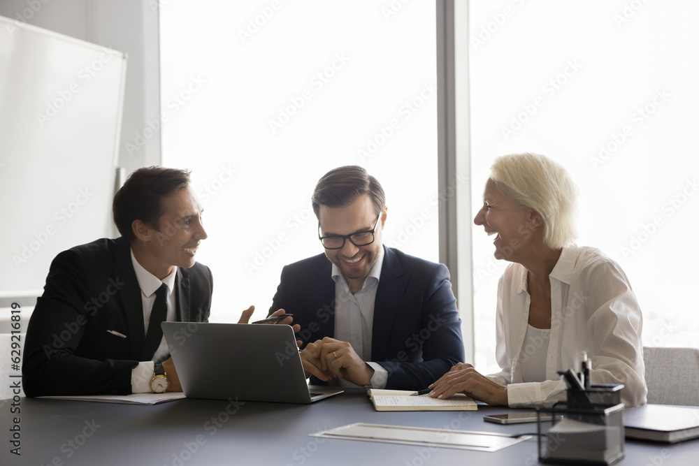 Canvas Prints Positive small business team brainstorming at laptop, discussing creative ideas, smiling, laughing. Cheerful younger and older colleagues having fun at office workplace