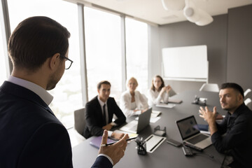 Back view of business leader man speaking to team of employees on office meeting. Presenter, speaker giving seminar, presentation, lecture to work group of colleagues on blurred background
