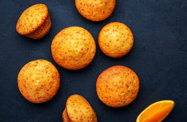 Sweet muffins with oranges and candied fruit on black table background, homemade pastries, top view