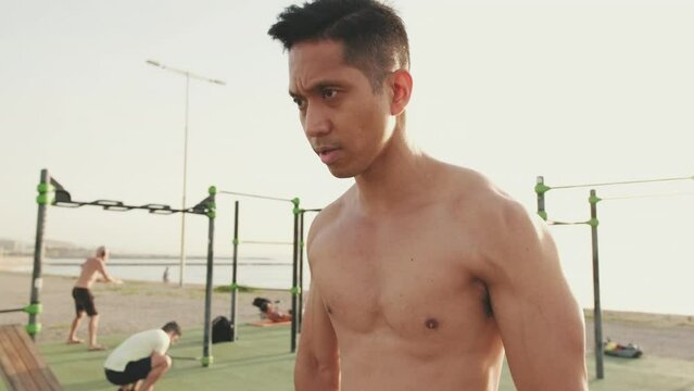 Young man doing push-ups on parallel bars on a sports ground by the sea