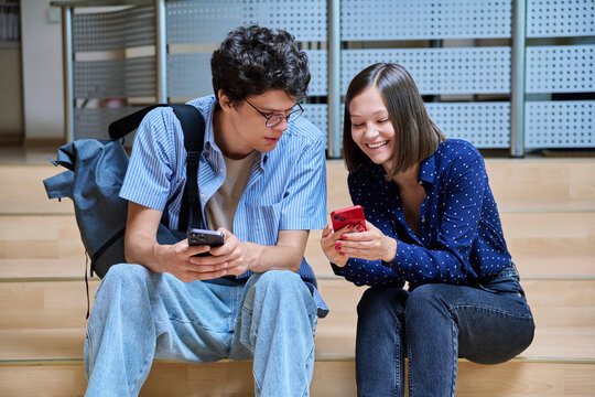 Friends college students guy and girl with smartphones inside educational building