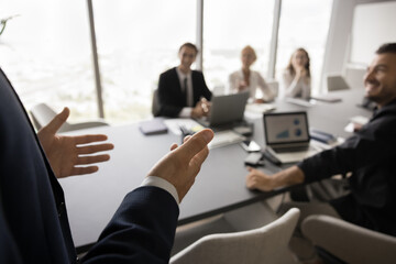 Presenter speaking team of colleagues, office employees sitting at meeting table, looking at presenter. Male business leader giving presentation. Close up of hands with audience in blurred background