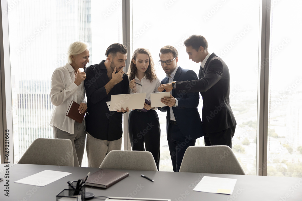 Canvas Prints Team of busy coworkers focused on gadget screen together, watching Internet content on laptop and tablet in business meeting room, standing close, discussing online presentation