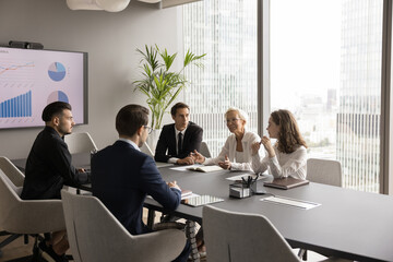 Confident senior business mentor woman talking to group of employees at office meeting table,...