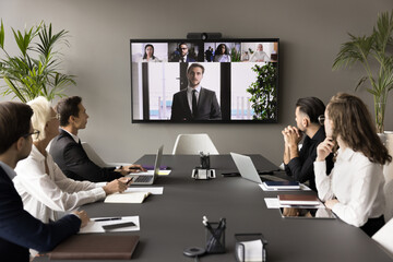 Business team and leader meeting online and offline, sitting at conference table, looking at...