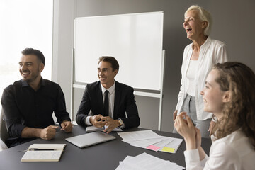 Cheerful younger and older coworkers meeting in boardroom for corporate education, training seminar, casually looking away, laughing, having fun, sitting at table, brainstorming