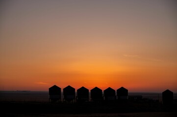 Grain bins silhouetted by the rising sun