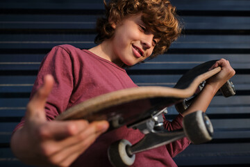 Glad boy examining skateboard near wall