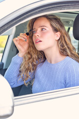 Young woman applying mascara in car