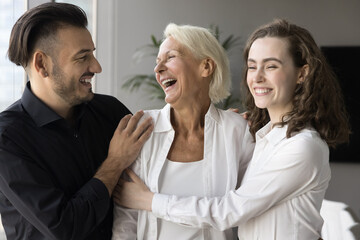 Happy elderly retired mom and adult son and daughter hugging with love, affection, talking, chatting, laughing, standing close, enjoying family relationships, celebrating mothers day
