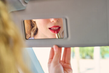 Crop young woman applying red lipstick against mirror in car - obrazy, fototapety, plakaty