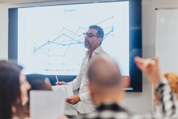 Middle-aged businessman explaining growth charts on presentation monitor during brainstorming