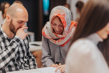 Obraz premium Woman in hijab pointing pointing at report, explaining and helping her hairless male coworker with his daily task at work