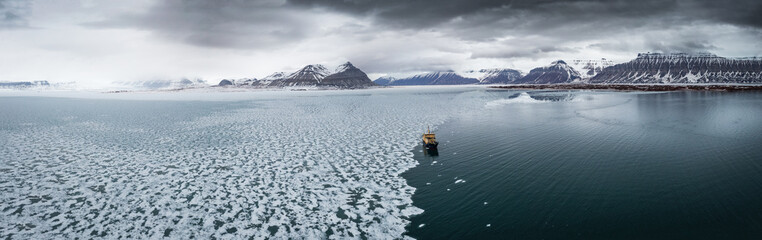 Drone shot of a ship in the ice in front of arctic landscape