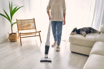 Crop woman cleaning floor with vacuum near cute lazy dog