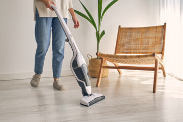 Crop unrecognizable female cleaning home with contemporary cordless vacuum cleaner - obrazy, fototapety, plakaty