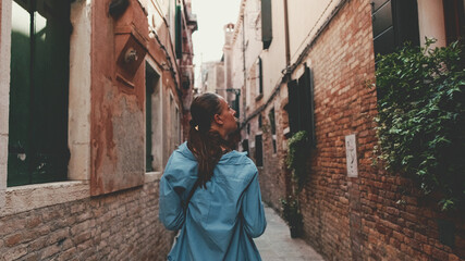 Fototapeta na wymiar Young woman walking along narrow street of old city, Venice, Back view