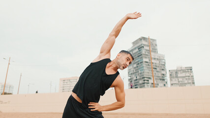 Mature man doing stretching exercises before main workout while standing on the beach