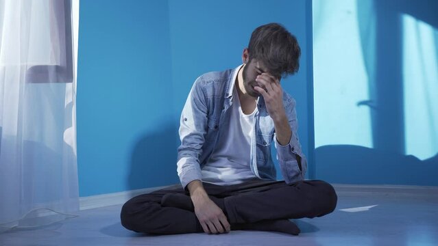 The man sitting on the ground is crying. Downhearted.