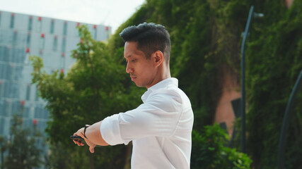 Young businessman is walking down the street and looking at his watch on modern building background
