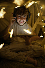 Cheerful boy sitting in blanket fort with tablet