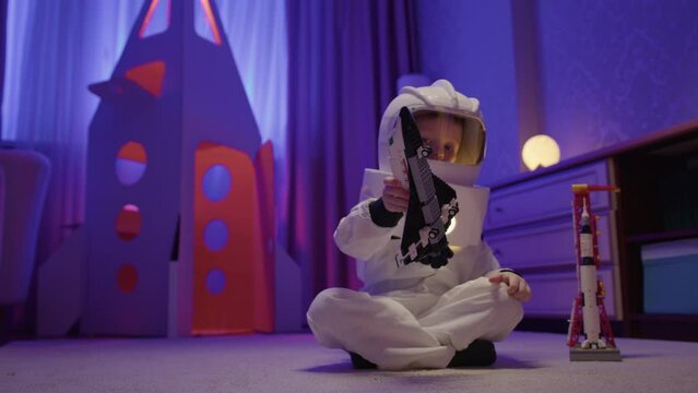 Small child in an astronaut spacesuit plays at home with toy Space Shuttle orbiter. Dream is to fly in space.
