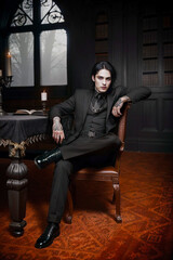 a goth man sitting in an antique chair in a Gothic library