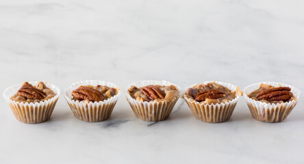 Sweet and salty caramel pecan tartlets all in a line against a light background.