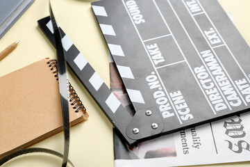 Movie clapper with newspaper, notebook and film on beige background, closeup