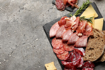 Slate plates with assortment of tasty deli meats, bread and cheese on grey background
