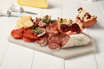 Board with assortment of tasty deli meats on white wooden background