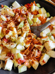 Stewed vegetables and silicone spatula with wooden handle in frying pan. Mixed Ingredients leek, carrot, zucchini, bell pepper. Process of cooking saute at home. Close-up. Selective focus.
