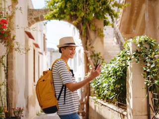 summer trip to Rhodes island Greece. Young Asian woman make photo on smartphone walks Street of Knights of Fortifications castle. female traveler visiting southern Europe. Unesco world heritage site