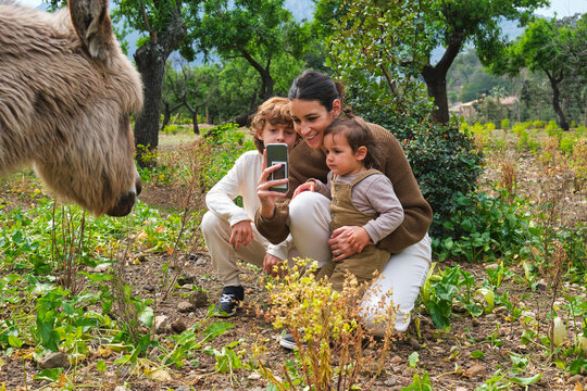 Happy mother with kids taking photo of cute donkey