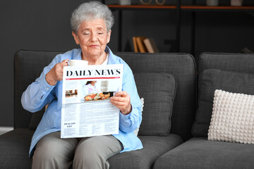 Senior woman with cup of coffee reading newspaper at home