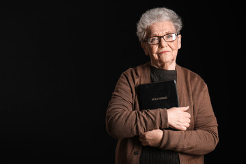 Senior woman with Holy Bible on black background