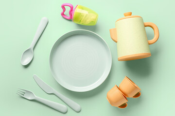 Different eating utensils for baby on pale green background