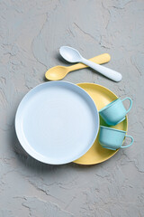 Cups with plates and spoons on grunge grey background