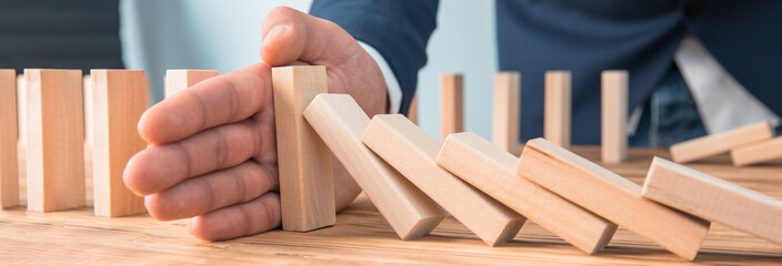 Businessman hand stopping falling wooden dominoes