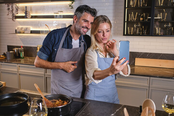 Happy diverse couple taking selfie on smartphone in kitchen