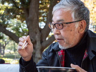 An older asian man eating noodles and soup with chopsticks - 629244483