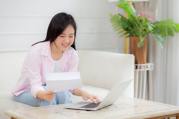 Young asian business woman working on laptop computer and looking graph and chart of report for profit on paper at home, businesswoman looking investment and income, data of infographic statistics.