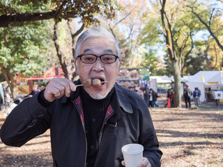 An older Japanese man eating dango and drinking coffee funnily