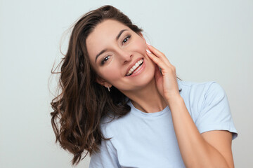 a photo of a positive young dark-haired Caucasian woman in a blue T-shirt, who smiling and touching her face with her hand. portrait of a beautiful model. Photo for advertising